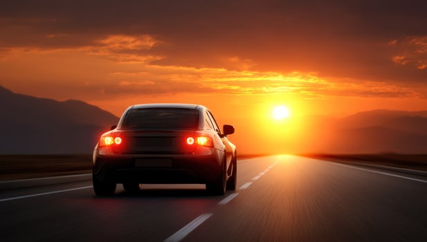 Car drives on road towards setting sun, scenic mountains, orange sky background photo