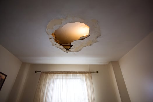 Damaged ceiling with hole reveals attic space in a beige room, interior photo
