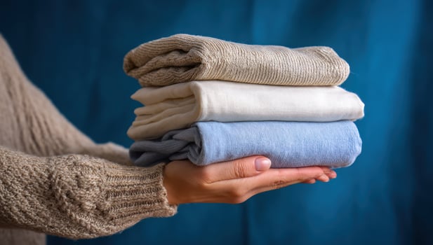 Hands holding neatly stacked folded clothes against a soft, draped background photo