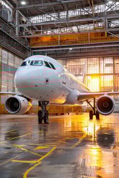 Airplane undergoes maintenance inside of a bright, large hangar at sunset photo