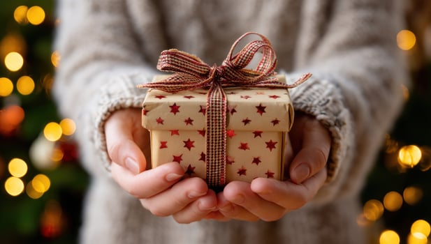 Hands presenting a wrapped gift box at home with tree and lights background photo