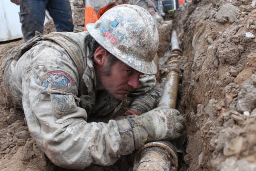 A soldier is working on a pipe in the dirt photo