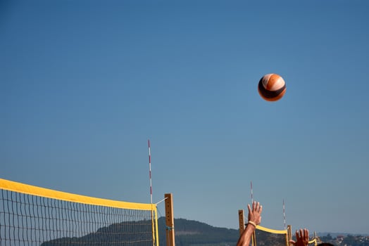Dynamic action during a beach volleyball match in Galicia with a ball suspended in the air and a blue sky in the background photo