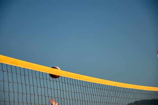 Beach volleyball players jump with arms outstretched to block a ball over the net photo