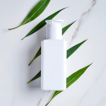 Elegant white cosmetic bottle with pump surrounded by fresh green leaves on a clean marble background product photography for skincare and wellness photo