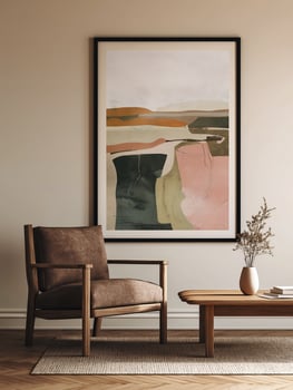 Modern living room corner with framed abstract art print on wall, brown armchair, wooden coffee table with vase and books, and neutral toned rug photo