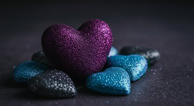 A Luminous Purple Glitter Heart Nestled Among Cool Blue and Black Hearts photo