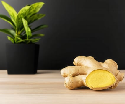 Fresh ginger root with slice showing vibrant yellow interior placed on wooden surface with green plant in black pot photo