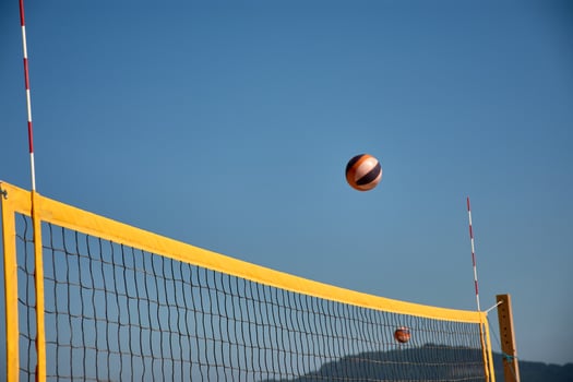 Sports action captured on the beach with a yellow volleyball net and a ball in mid-flight in the background Natural scene photo