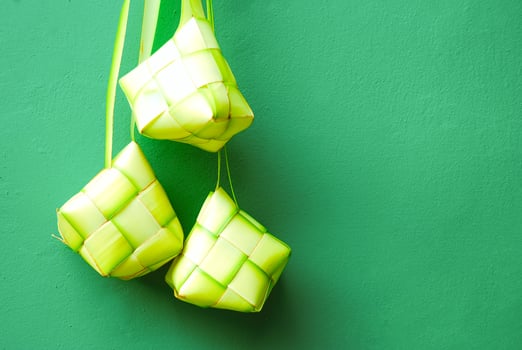Traditional woven ketupat rice dumplings hanging against a vibrant green backdrop. Ideal for Eid, festive food, or Southeast Asian culture themes. photo