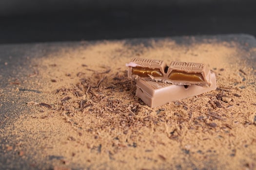 cut of chocolate stuffed with caramel chocolate bar lies on the cocoa on a black background with place for text and a copy of the day of chocolate photo