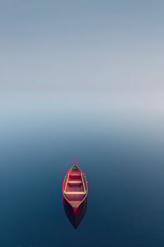 Serene red rowboat rests silently atop tranquil blue water with a clear reflection photo