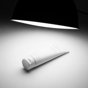 A tube of cream sits on a table in front of a lamp photo