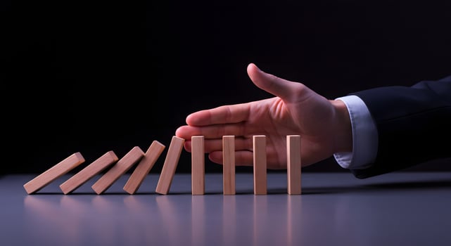 A hand reaching out to stop a domino from falling photo