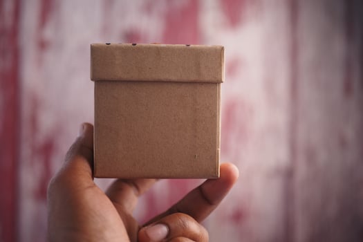 Hand holding a small brown box against a textured background photo
