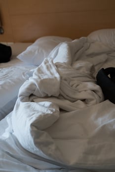An unmade bed in a bedroom with crumpled bed sheet, a blanket. photo