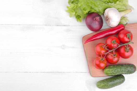 Many different vegetables including, tomatoes, peppers, cucumbers, onions, garlic and lettuce on a white wooden background. Top view photo