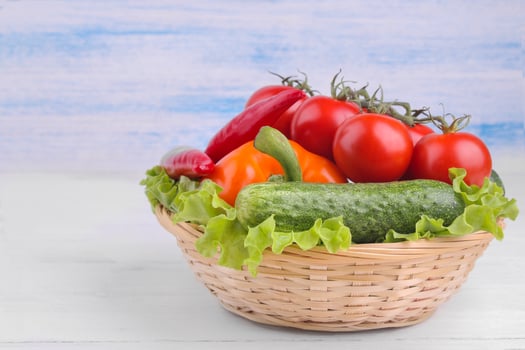 Many different vegetables in the basket including, tomatoes, pepper, cucumbers and lettuce on a white and blue wooden background. photo