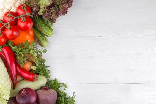 Many different vegetables include beets, cabbage, zucchini, carrots, tomatoes, peppers, onions, garlic, and cucumbers and lettuce on a white and wooden background. top view photo