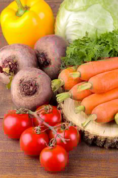 Many different vegetables include cabbage, tomatoes, peppers, carrots and beets on a wooden stand on a brown wooden background. photo