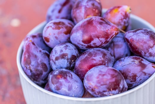 Ripe plums in a bowl on a wooden table close up photo