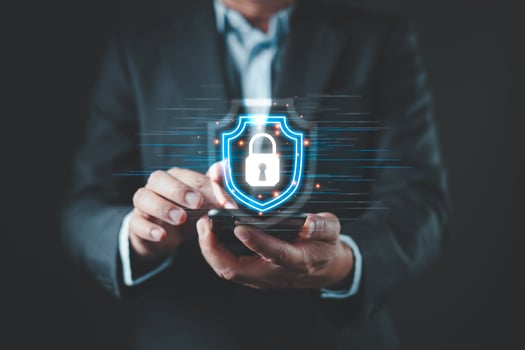 A business professional uses a smartphone with a glowing shield icon displaying a lock, symbolizing secure cyber data protection through advanced technology and modern digital defense systems. photo