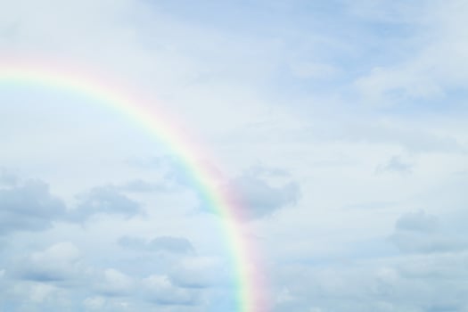 A rainbow is seen in the sky above a beach photo