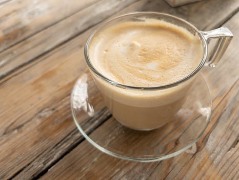 Glass cup of coffee on rustic wooden table in outdoor cafe, photo