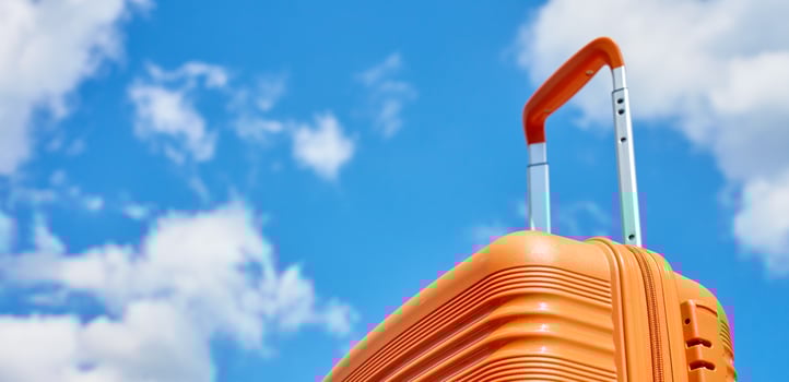 Orange suitcase stands against blue sky with white clouds. Concept of travel, vacation and summer adventure photo