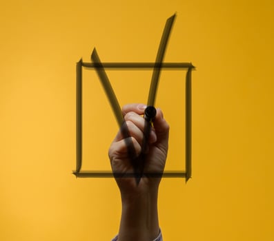 Human hand holding marker and drawing big black check mark inside drawn square. photo