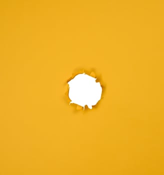 A round hole with jagged edges is made in a sheet of bright yellow paper. photo