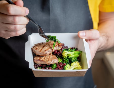 Hearty lunch bowl with seared medallions, broccoli florets, and ruby beans in a compostable takeaway container photo