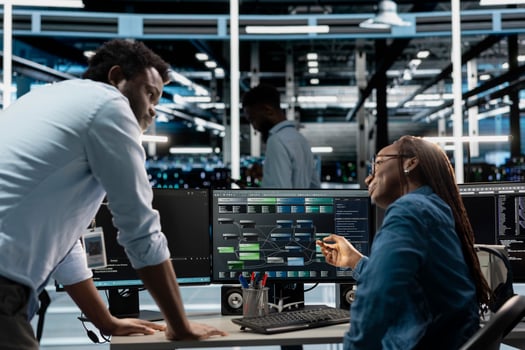 Supervisor checking work done by engineer programming in server hub housing infrastructure storing datasets. African american team leader overseeing IT specialist repairing data center racks photo