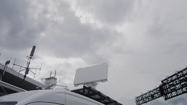 A vehicle parked on an urban street under a cloudy sky. Communication antennas and a large blank billboard are visible, hinting at technology integration in the city. photo