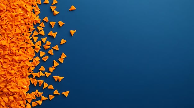 A Scattered Pile of Small Orange Cheesy Snacks on a Blue Background. photo