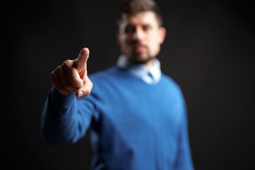 Person in blue sweater pointing with finger in dramatic lighting against black background photo