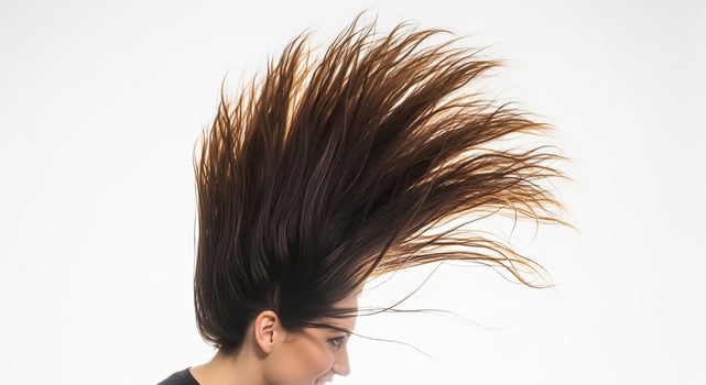 A woman with flowing brown hair tossed upwards against a white background, capturing a dynamic and energetic beauty concept. photo