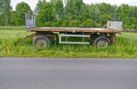 Old wooden trailer standing empty in grassy rural field photo