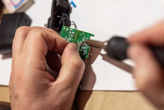 man solders wiring in the electronic circuit board of the device photo