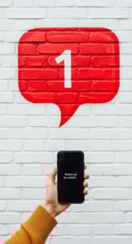Hand holding black smartphone with swipe to unlock message below red notification bubble on white brick wall photo
