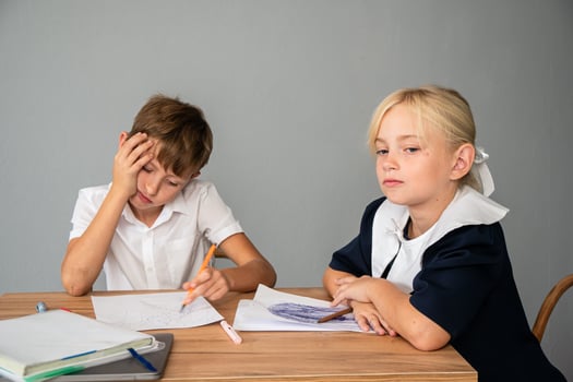 Children School Homework Frustration - Two kids sitting at a table doing schoolwork, one looks frustrated while the other is focused. photo