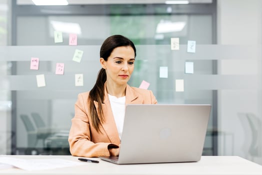 Busy elegant middle-aged businesswoman using a laptop in a corporate office. Mature professional female manager thinking about a project while looking at the computer screen. photo