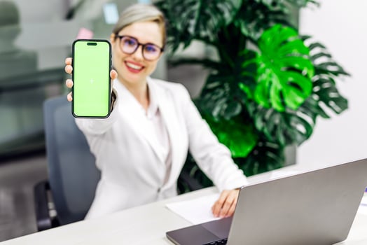 In a modern office, a young woman holds up a phone with a green screen. Perfect for showcasing digital ads, interactive content. photo