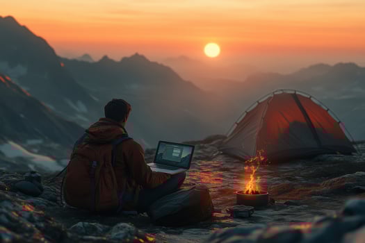 A man sitting on a rock with a laptop and a tent photo