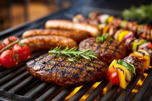 Delicious grilled steaks, sausages and vegetable skewers cooking on barbecue grill photo