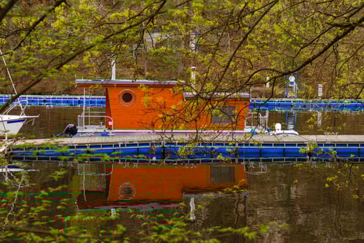 Floating house with round window docked at marina - reflection in water through spring branches photo