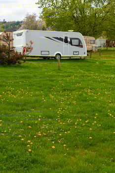 Modern caravan parked on vibrant green meadow with yellow dandelions at spring campsite photo