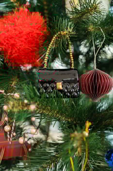 Close-up of a shiny black handbag-shaped ornament hanging on a plastic artificial Christmas tree photo