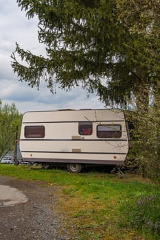 Vintage caravan parked near river under fir tree - peaceful spring camping scene in rural nature photo