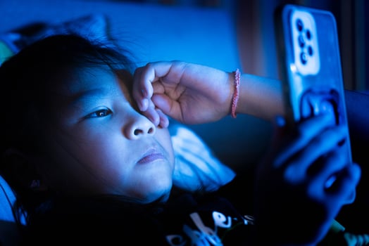 Little Asian girl using smartphone in bed at night, screen light on face photo